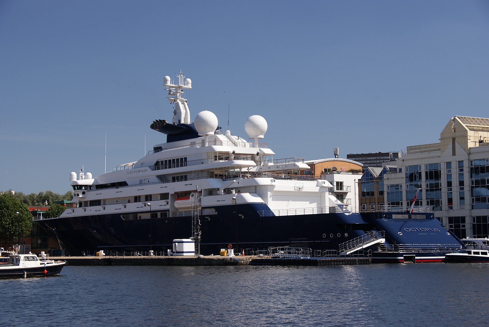 Dark-hulled explorer yacht Octopus moored at a quay in front of office buildings
